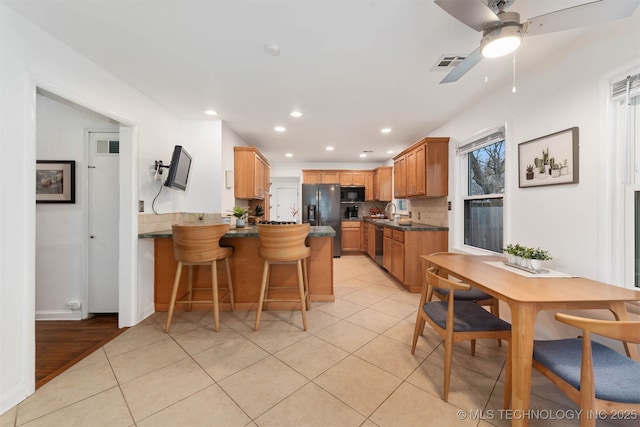 kitchen featuring a breakfast bar, black appliances, backsplash, light tile patterned floors, and kitchen peninsula