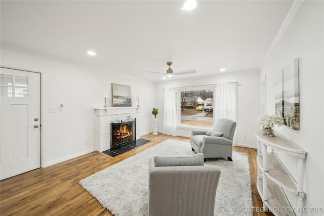 living room with crown molding, ceiling fan, wood-type flooring, and a brick fireplace