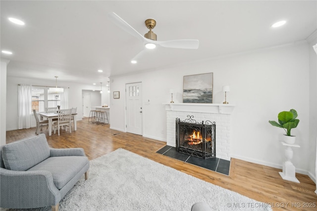 living room featuring ceiling fan, wood-type flooring, a fireplace, and ornamental molding