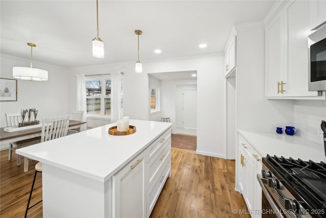 kitchen with a kitchen island, appliances with stainless steel finishes, decorative light fixtures, white cabinetry, and light hardwood / wood-style floors