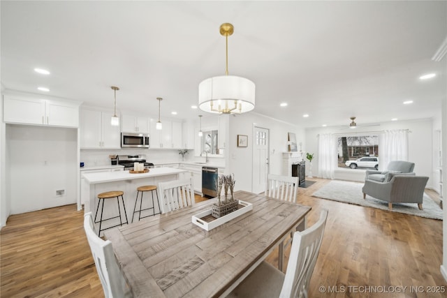 dining area featuring sink, a fireplace, ceiling fan, and light wood-type flooring