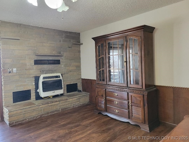 living room with dark hardwood / wood-style flooring, heating unit, a textured ceiling, and wood walls