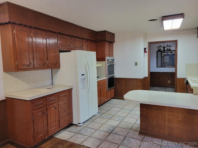 kitchen with multiple ovens, white refrigerator with ice dispenser, wooden walls, and a textured ceiling