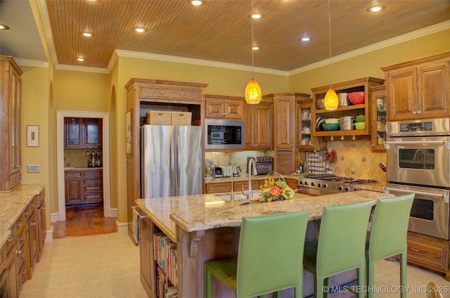 kitchen featuring sink, a kitchen bar, light stone counters, stainless steel appliances, and a center island with sink