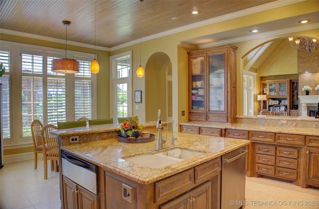 kitchen with pendant lighting, sink, crown molding, light stone counters, and a center island with sink