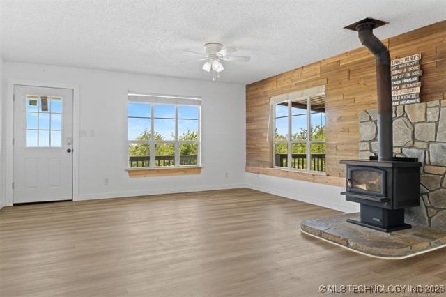 unfurnished living room with hardwood / wood-style flooring, ceiling fan, wooden walls, a textured ceiling, and a wood stove