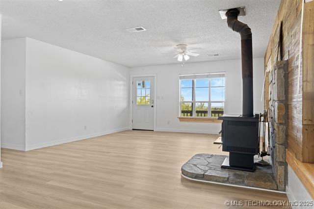 unfurnished living room featuring ceiling fan, light wood-type flooring, a textured ceiling, and a wood stove