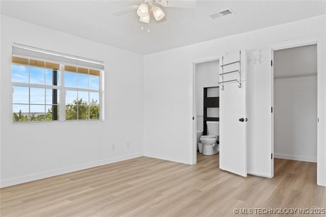 unfurnished bedroom with connected bathroom, a spacious closet, a closet, and light wood-type flooring