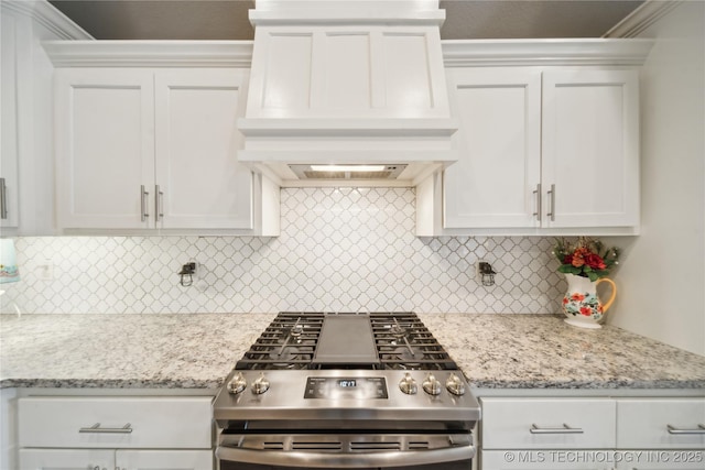 kitchen with light stone counters, premium range hood, stainless steel range with gas stovetop, and white cabinets