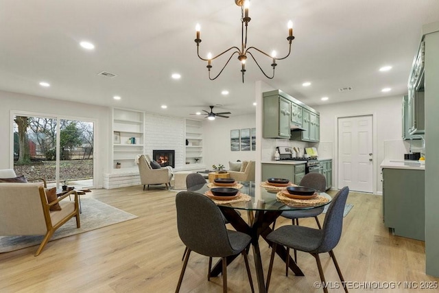 dining space featuring a brick fireplace, built in shelves, light hardwood / wood-style flooring, and ceiling fan