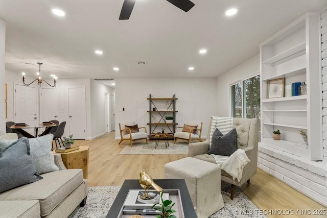 living room with ceiling fan with notable chandelier and light hardwood / wood-style flooring