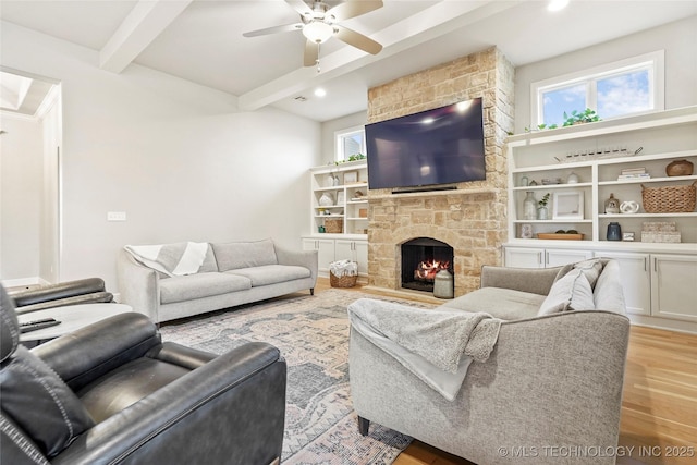 living room with beamed ceiling, a healthy amount of sunlight, a stone fireplace, and light hardwood / wood-style flooring