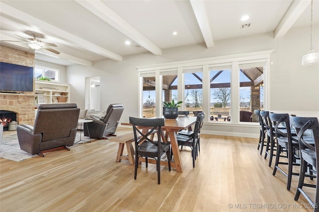 dining space with a healthy amount of sunlight, a stone fireplace, light hardwood / wood-style floors, and beam ceiling