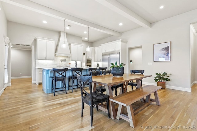 dining area featuring sink, light hardwood / wood-style flooring, and beamed ceiling