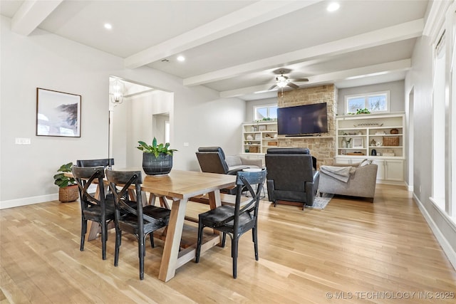 dining space featuring beam ceiling, ceiling fan, a large fireplace, and light wood-type flooring