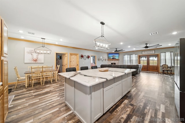 kitchen with white cabinetry, hanging light fixtures, dark hardwood / wood-style floors, a center island, and light stone countertops