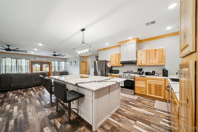 kitchen featuring a breakfast bar area, a center island, light brown cabinets, appliances with stainless steel finishes, and pendant lighting