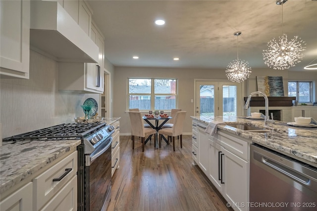 kitchen with wall chimney exhaust hood, appliances with stainless steel finishes, decorative light fixtures, and white cabinets