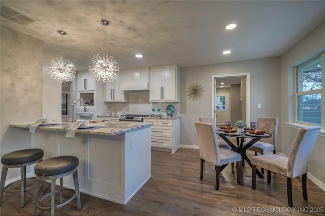 kitchen with white cabinetry, light stone counters, pendant lighting, and stainless steel range oven