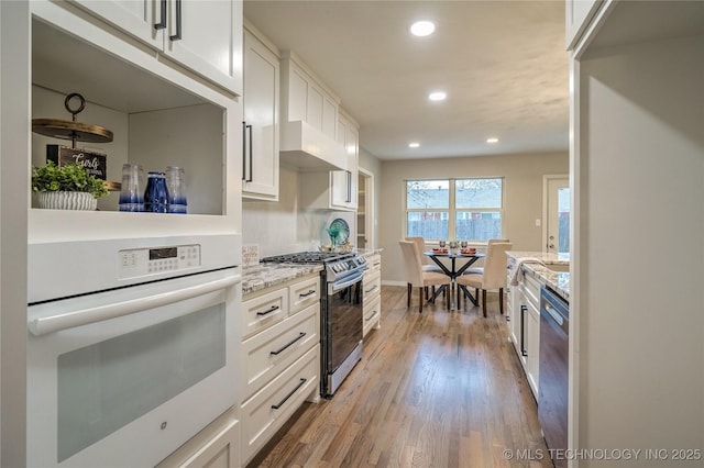 kitchen with light stone countertops, light hardwood / wood-style floors, white cabinets, and appliances with stainless steel finishes