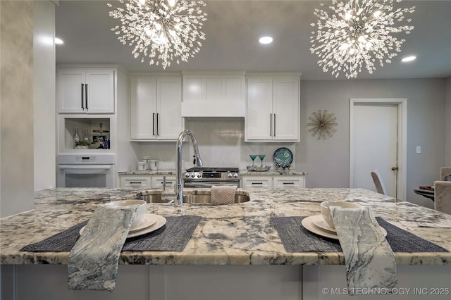 kitchen featuring white cabinetry, a chandelier, oven, and light stone counters