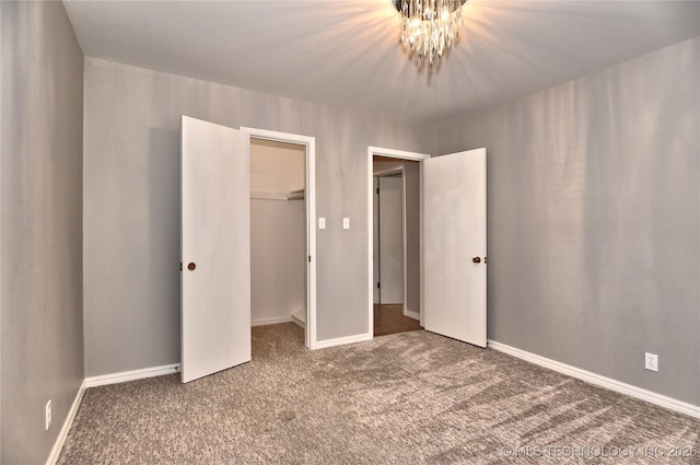 unfurnished bedroom with a notable chandelier, a spacious closet, a closet, and carpet