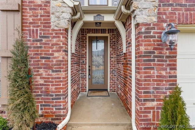 view of exterior entry featuring a garage and brick siding