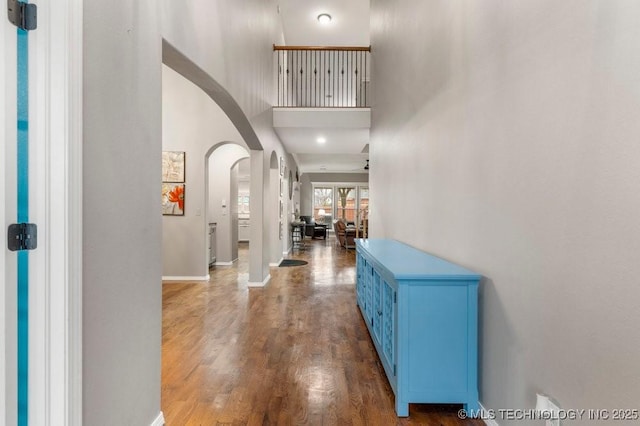 foyer with wood finished floors, arched walkways, baseboards, and a high ceiling