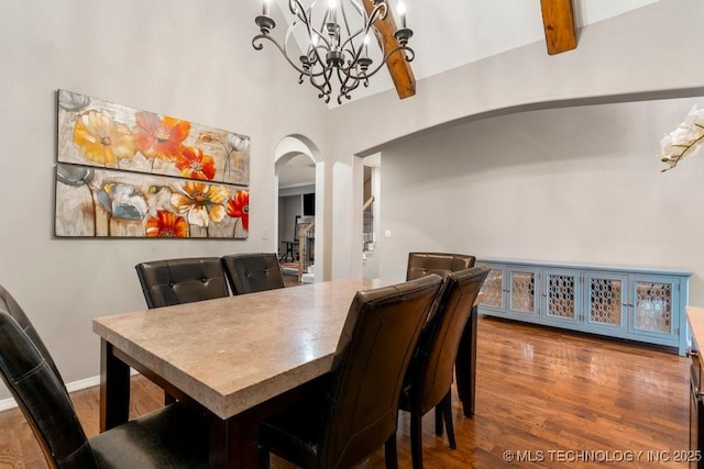 dining space with arched walkways, wood finished floors, beam ceiling, and baseboards