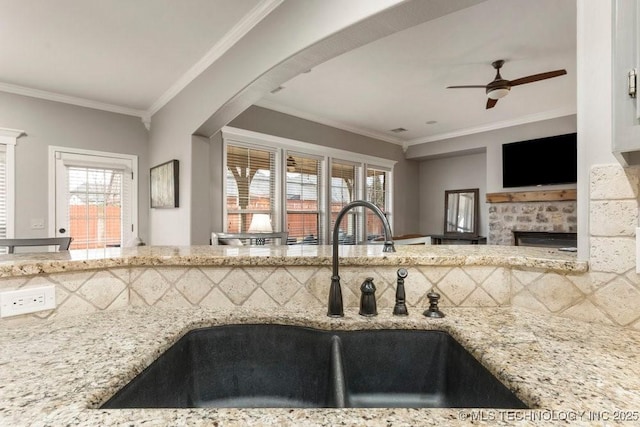 kitchen with a sink, light stone counters, ceiling fan, and crown molding