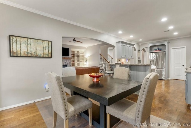 dining room with hardwood / wood-style flooring, a fireplace, ornamental molding, and ceiling fan