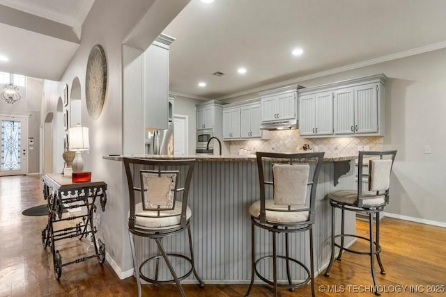 kitchen featuring arched walkways, a breakfast bar, a peninsula, under cabinet range hood, and backsplash