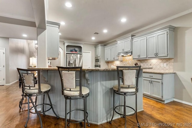 kitchen featuring a breakfast bar area, wood finished floors, appliances with stainless steel finishes, gray cabinets, and crown molding