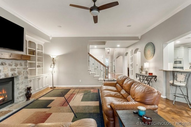 living room with arched walkways, a fireplace, wood finished floors, and crown molding