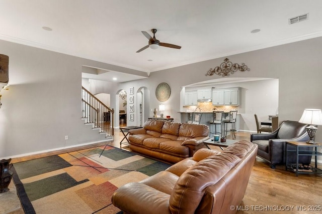 living room featuring arched walkways, visible vents, baseboards, stairs, and crown molding