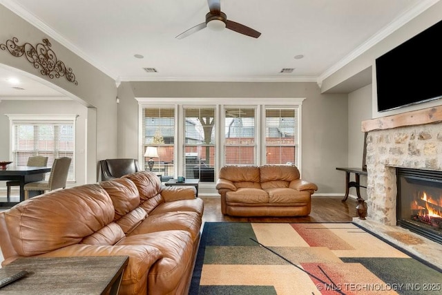 living room with crown molding, ceiling fan, wood-type flooring, and a stone fireplace