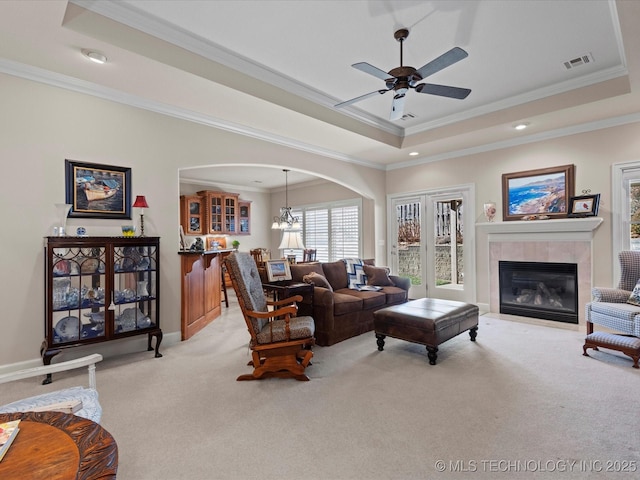 carpeted living room with crown molding, a tray ceiling, a tile fireplace, and ceiling fan