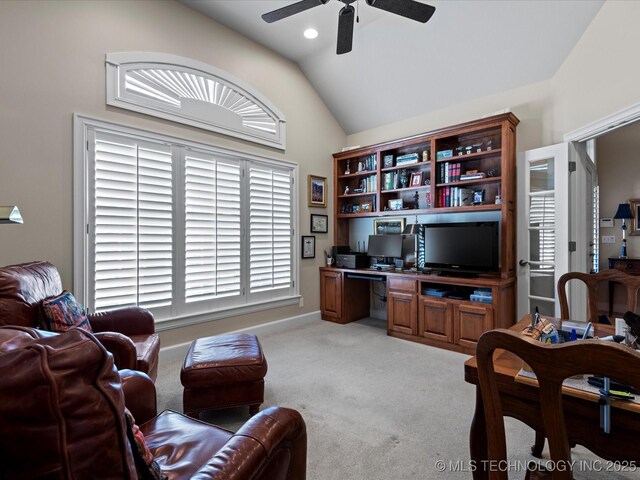 carpeted living room with ceiling fan, built in desk, and vaulted ceiling