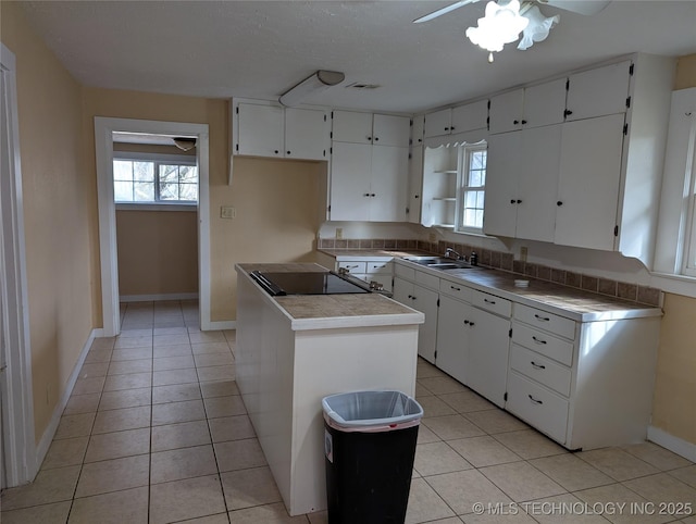 kitchen with sink, light tile patterned floors, a center island, a wealth of natural light, and white cabinets