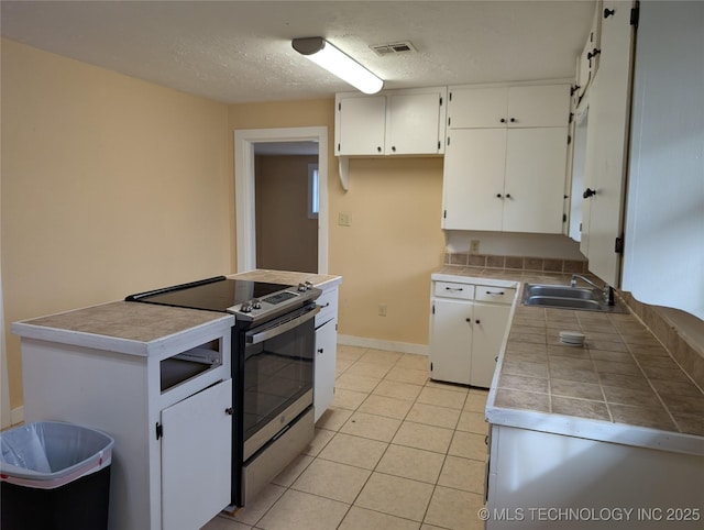 kitchen featuring sink, light tile patterned floors, stainless steel range with electric stovetop, a textured ceiling, and white cabinets