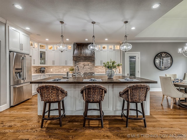 kitchen featuring white cabinets, high end refrigerator, a breakfast bar, and a large island with sink