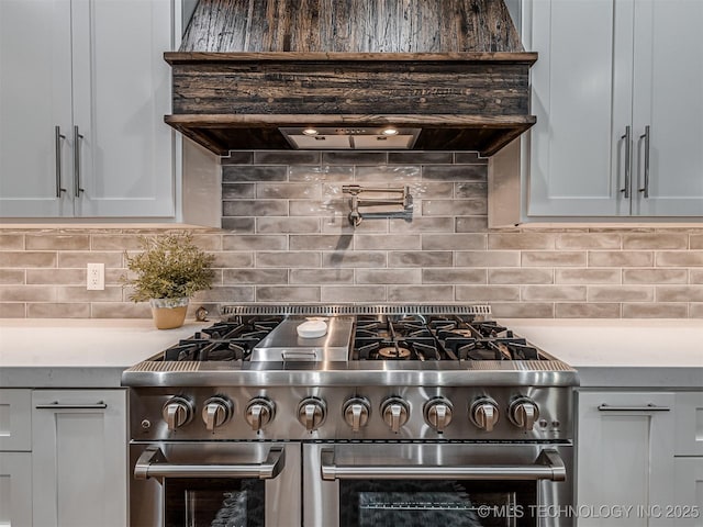 kitchen with tasteful backsplash, gray cabinets, range with two ovens, and custom range hood