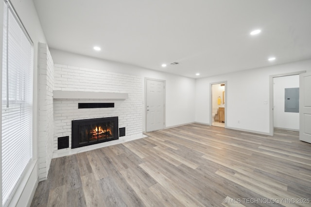 unfurnished living room featuring a fireplace, electric panel, and light hardwood / wood-style floors