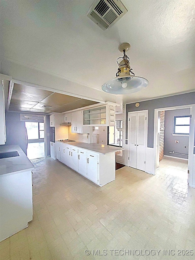 kitchen with black electric stovetop, hanging light fixtures, kitchen peninsula, and white cabinets