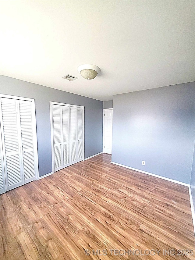 unfurnished bedroom featuring hardwood / wood-style floors and two closets