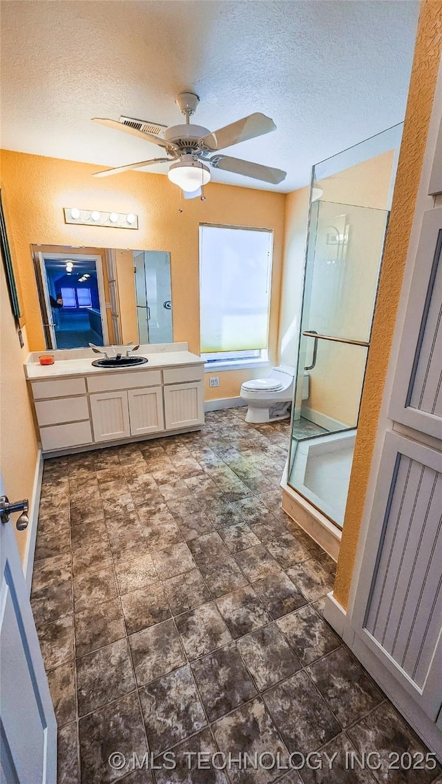 bathroom featuring toilet, a textured ceiling, vanity, a shower with door, and ceiling fan