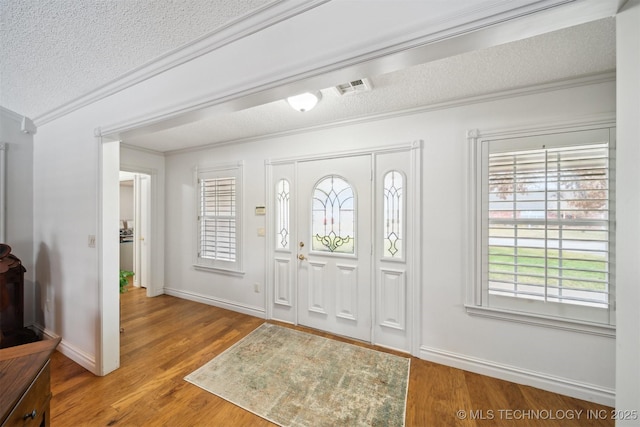 foyer entrance with wood-type flooring, ornamental molding, and a textured ceiling