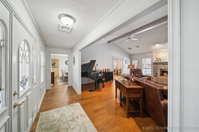 entrance foyer with a stone fireplace, lofted ceiling with beams, a textured ceiling, ornamental molding, and hardwood / wood-style floors