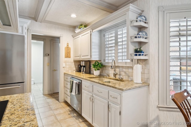 kitchen with sink, ornamental molding, stainless steel appliances, light stone countertops, and white cabinets