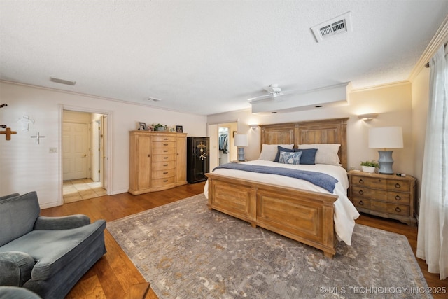 bedroom featuring a walk in closet, ornamental molding, hardwood / wood-style floors, and a textured ceiling